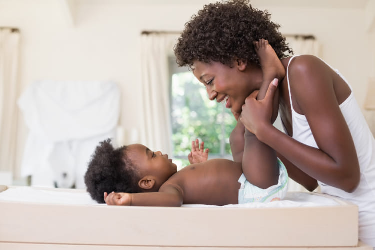 Femme afro-américaine qui sourit en regardant son bébé, tout en changeant sa couche.